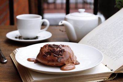 巧克力甜点在开放的书在后台茶壶和茶杯

